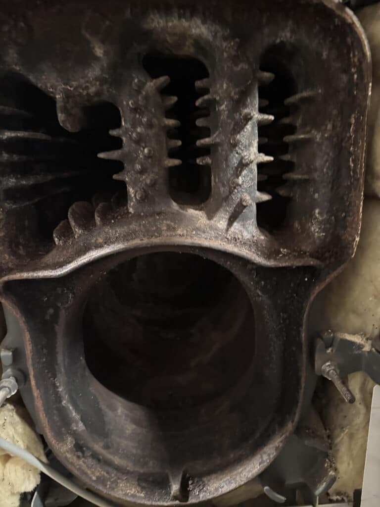 Intérieur en fonte rouillée d'un corps de chaudière ou fourneau, montrant une grande ouverture inférieure et des ailettes de transfert thermique.