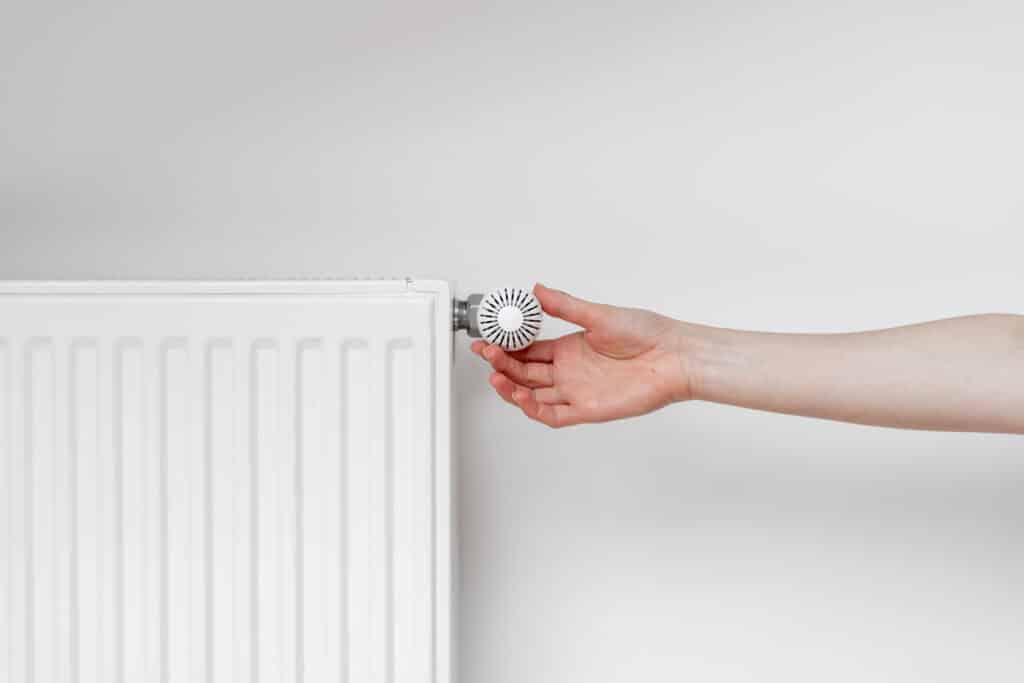 Main réglant un thermostat blanc sur un radiateur blanc pour ajuster la température de chauffage et économiser l'énergie.