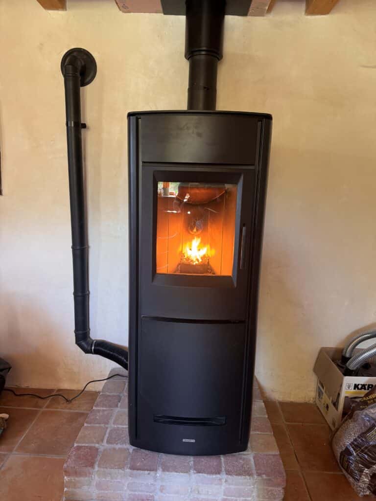 Poêle à granulés Piazzetta noir en fonctionnement, flammes visibles, raccordé à un conduit d'évacuation noir mural.